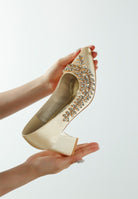 Beige satin embellished heel held in hands, close-up view
