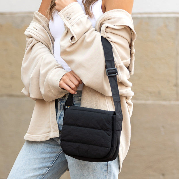Person holding a black crossbody bag against a neutral background