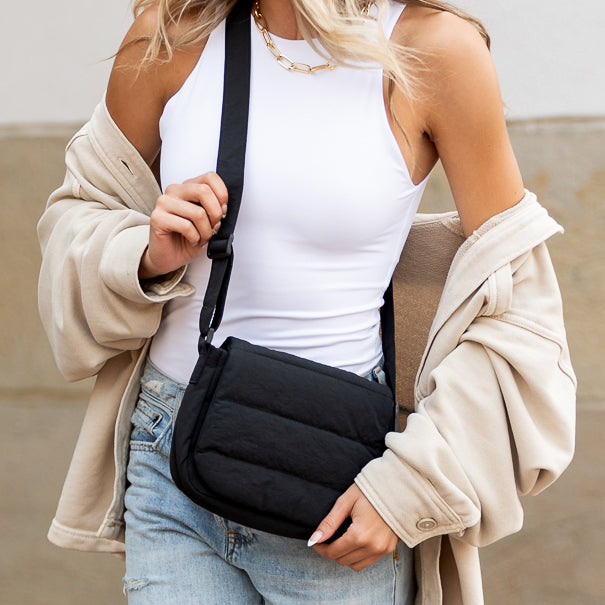 Person wearing a black crossbody bag with a neutral background