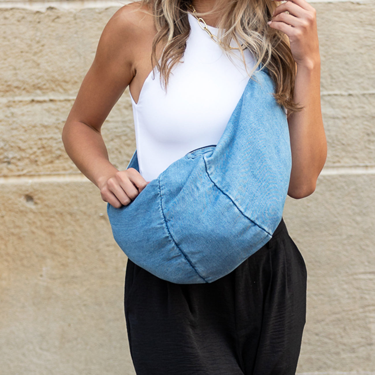 AVAH-washed denim crescent sling bag worn crossbody with adjustable strap