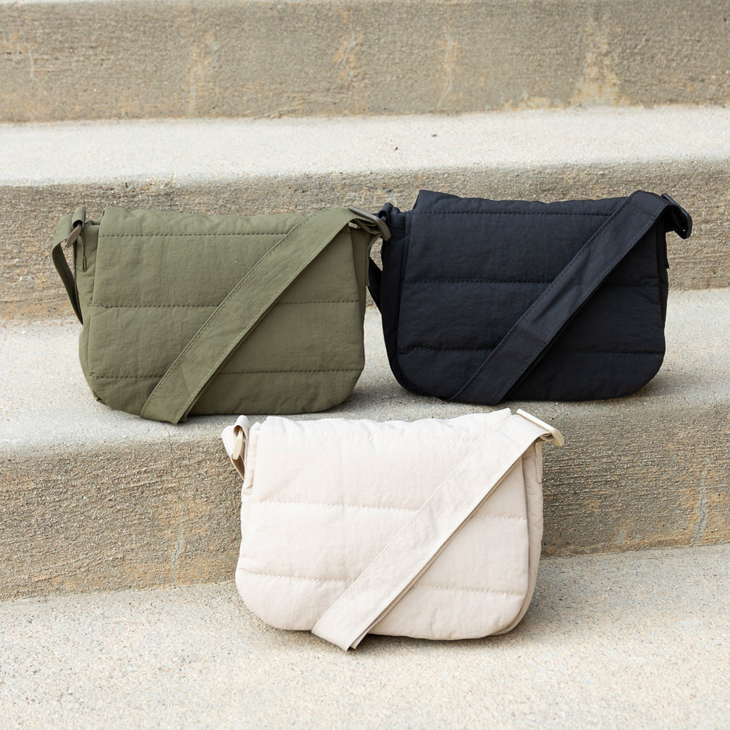 Three foldover crossbody bags in green, black, and beige on a stone surface.