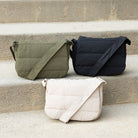 Three foldover crossbody bags in green, black, and beige on a stone surface.