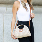 Straw crossbody bag with vegan leather and fixed top handle and removable crossbody strap complete with a fold over clasp and gold hardware, in straw front view