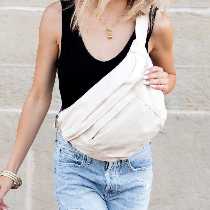 Person wearing a cream canvas oversized crossbody sling bag with a neutral background