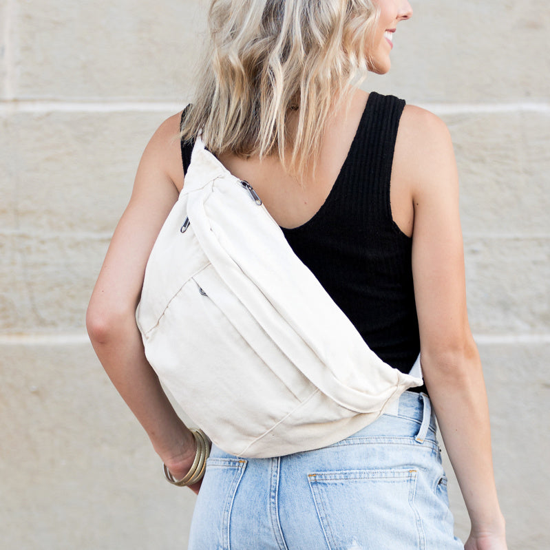 Person wearing a cream canvas oversized crossbody sling bag over one shoulder against a neutral background