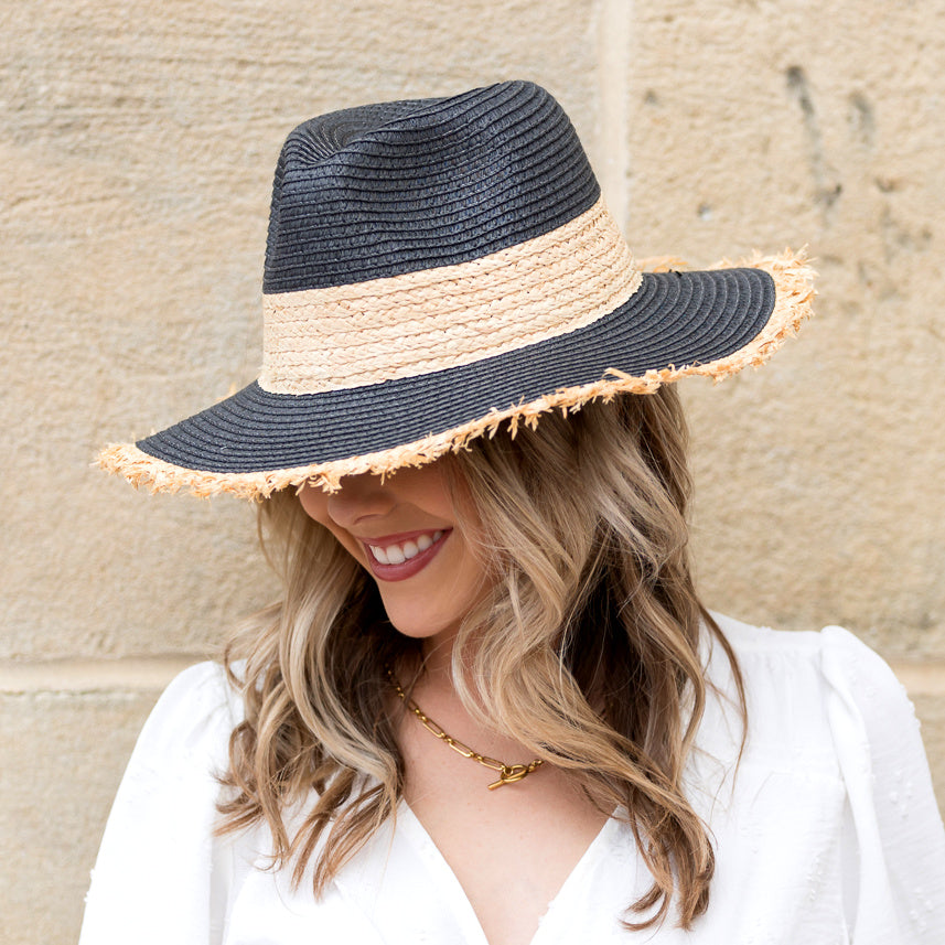 Woman wearing a black straw sun hat with natural rattan band and frayed fringe brim