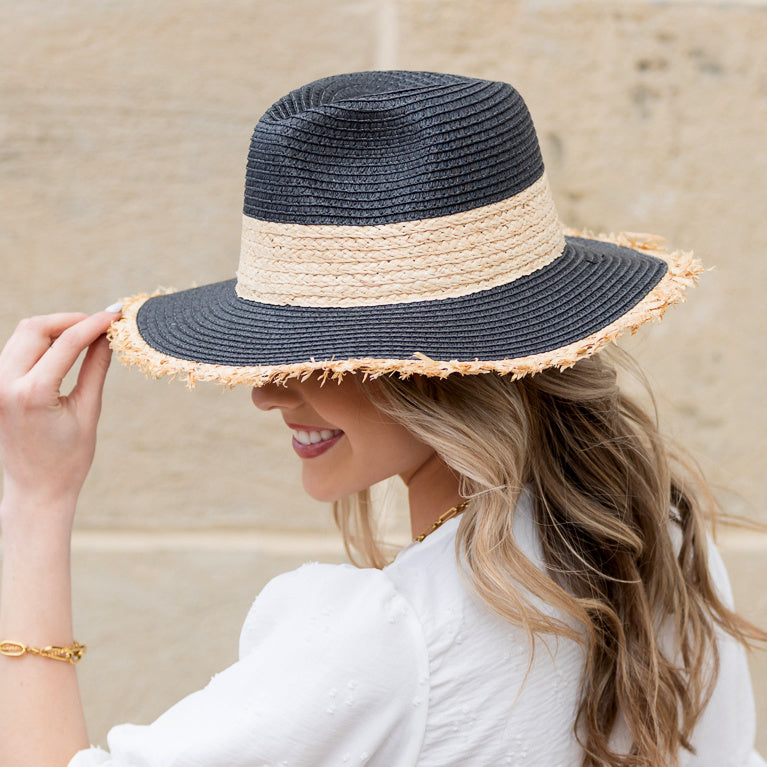 Woman wearing a black straw sun hat with natural rattan band and frayed fringe brim