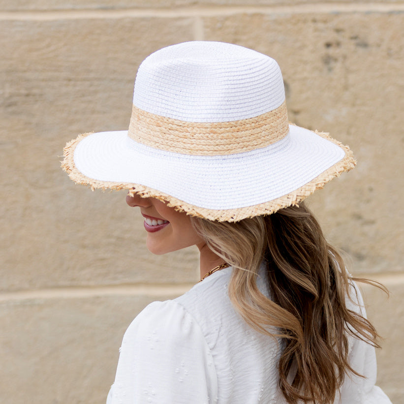 Side view of woman wearing a white straw sun hat with natural rattan band and frayed fringe brim
