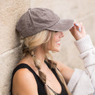 Woman wearing a cotton twill gray cap against a stone wall