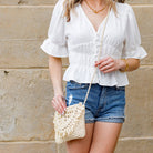 Model wearing cream woven straw crossbody with fringe flap detail, styled with a white blouse and denim shorts-AVAH