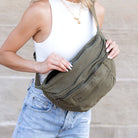 Person holding an olive green canvas oversized crossbody sling bag with a neutral background