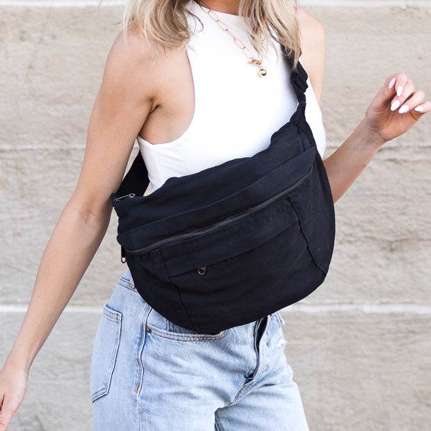 Person wearing a black canvas oversized crossbody sling bag with a neutral background