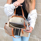 Person holding a beige  canvas handbag with brown straps showing its interior against a stone wall.