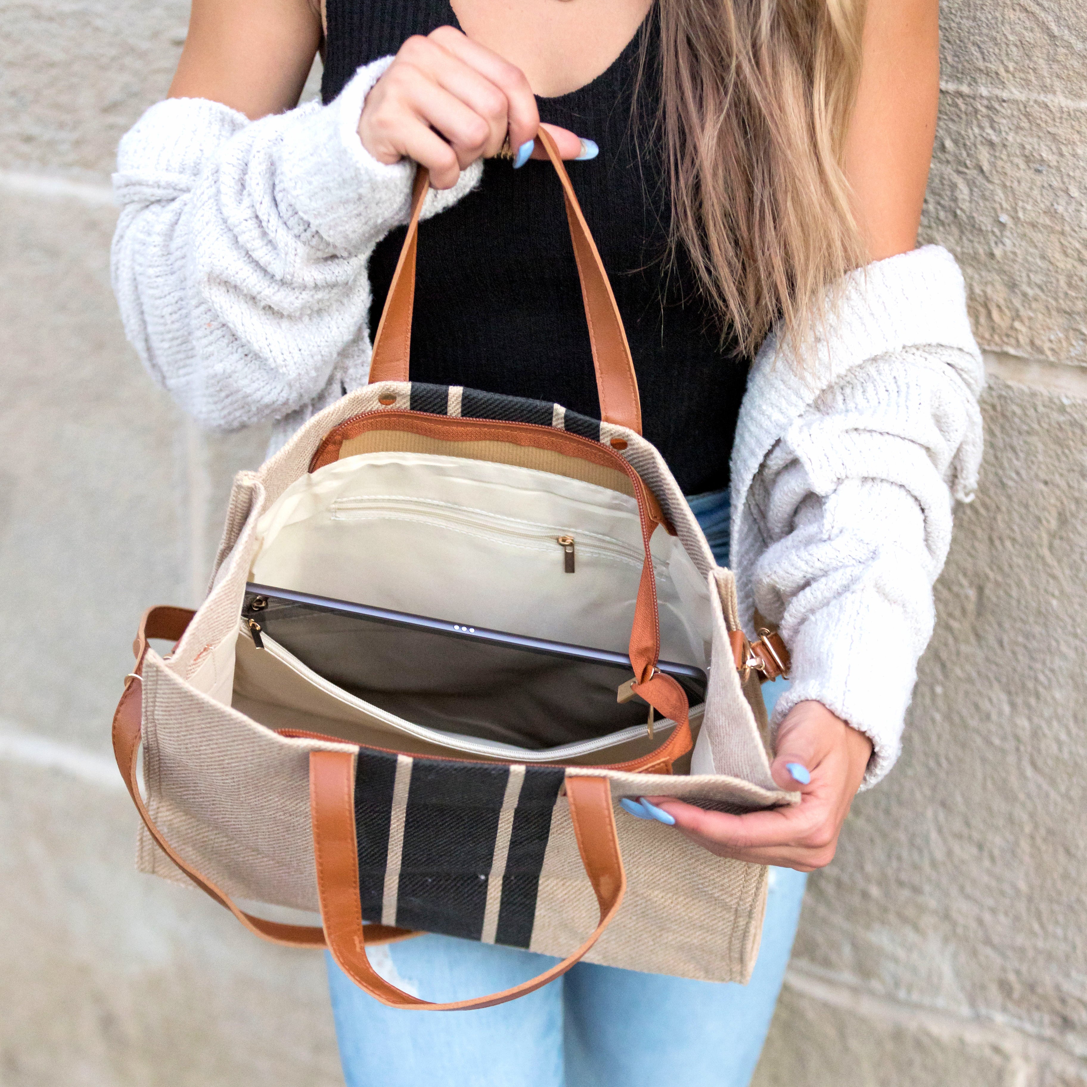 Person holding a beige  canvas handbag with brown straps showing its interior against a stone wall.