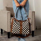 Woman holding cognac checkered hobo bag by its shoulder strap.