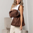 Woman carrying mocha suede-look hobo shoulder bag with matching pouch indoors.