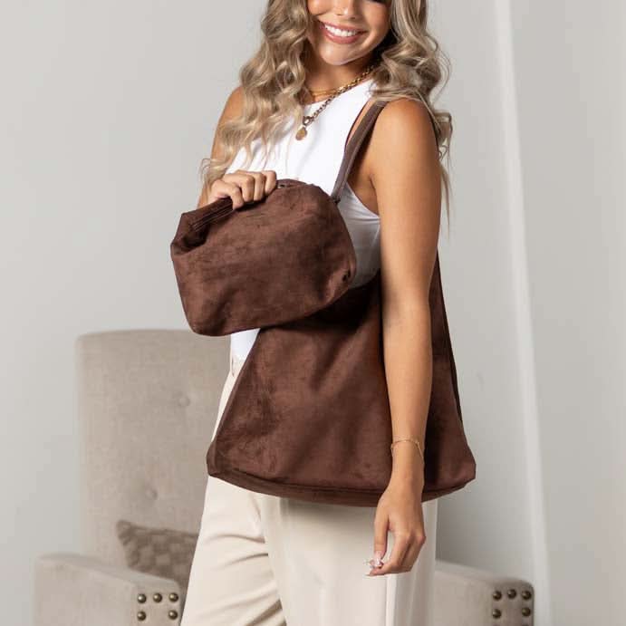 Woman carrying mocha suede-look hobo shoulder bag with matching pouch indoors.