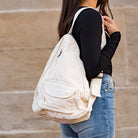 Person wearing a cream canvas single strap backpack against a beige wall