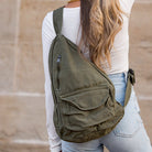 Person wearing an olive green sling bag with a neutral background