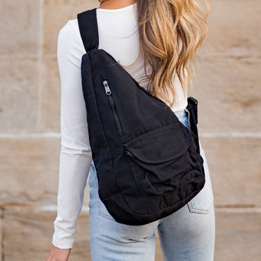 Person wearing a black sling bag against a beige wall