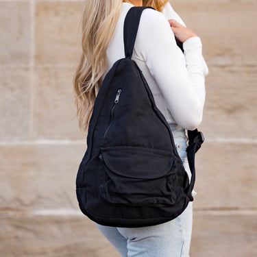 Person wearing a black backpack outdoors on a light-colored surface
