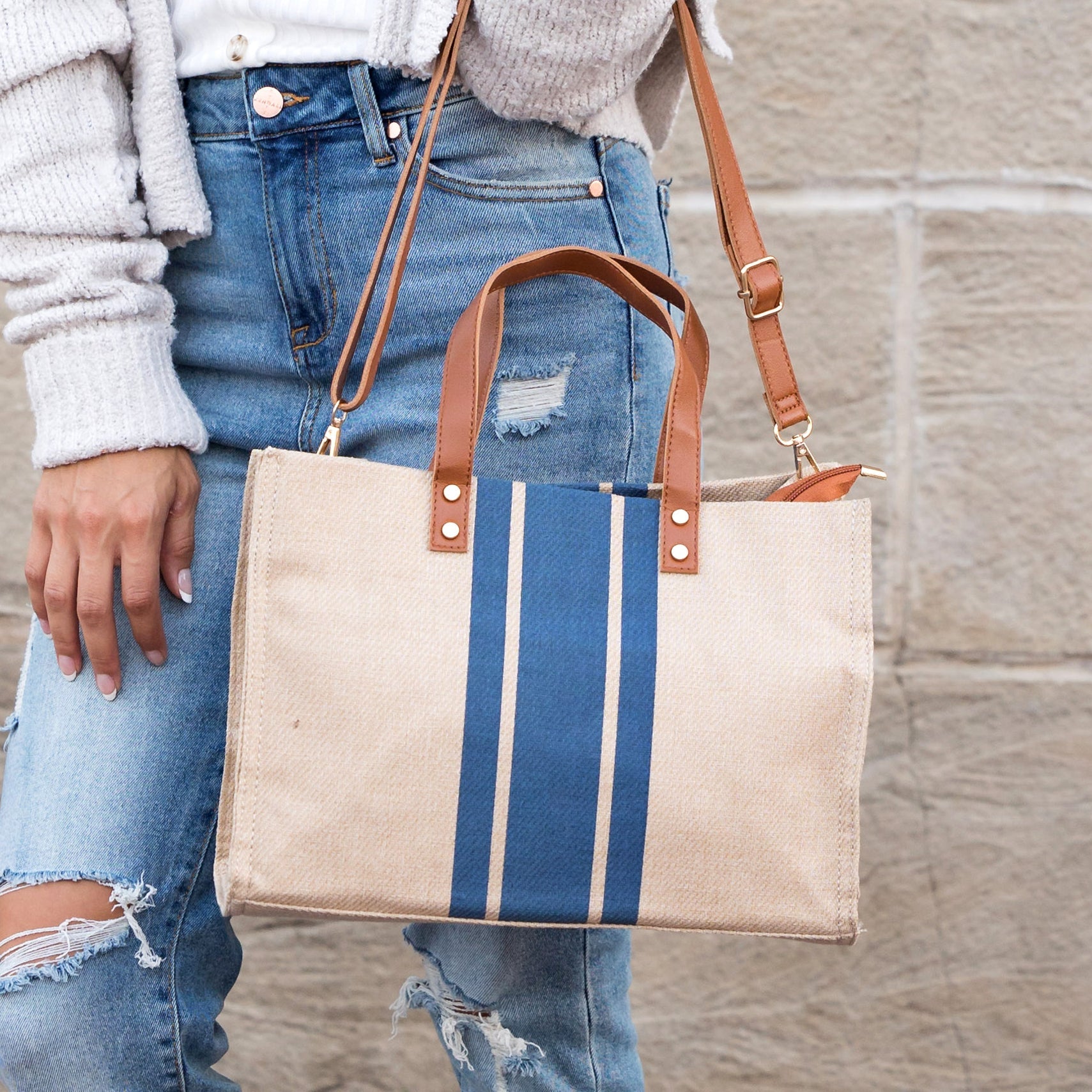 Person holding a tote bag with blue stripes against a stone wall.