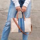 Person holding a striped tote bag with a brown strap against a wooden background
