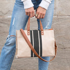 Person holding a striped tote bag with brown leather straps against a stone wall background