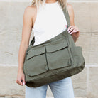 Person holding an olive green shoulder messenger bag against a stone wall background