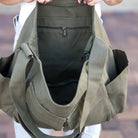 Olive green bag interior with multiple compartments held by a person against a blurred background