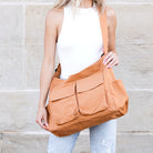 Person holding a camel  canvas messenger bag against a stone wall background
