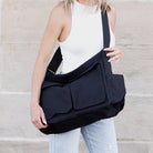 Person holding a black shoulder messenger bag against a neutral background