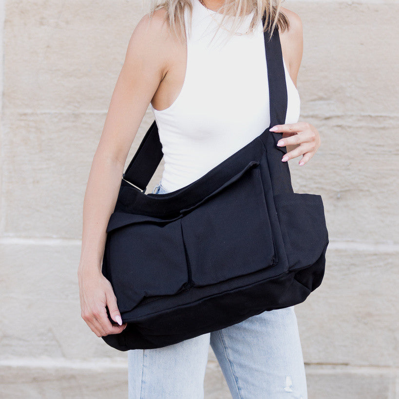 Person holding a black shoulder messenger bag against a neutral background