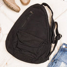 Black sling bag on a light wooden surface with a shoe and jeans in the background
