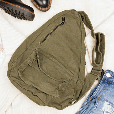 Green shoulder bag on a light wooden surface with shoes and jeans.