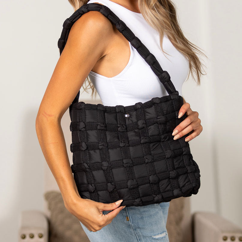 Person holding a black basket weave puff tote bag against a neutral background