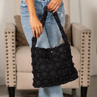 Person holding a black basket weave puff tote bag in a living room setting