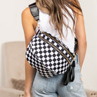 AVAH-Woman wearing a black and white checkered chic oversized sling bag with double zips and multiple pockets on a neutral background