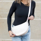 Person wearing a black long-sleeve top and blue jeans, holding a bone-colored vegan leather crossbody bag