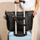 Black quilted travel bag with handle attached to a blue suitcase.