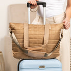 Person holding a Mocha quilted bag over a light blue suitcase.