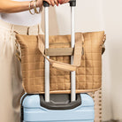 Person holding a Mocha quilted bag with a handle over a blue suitcase.