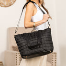 Person holding a black quilted travel tote in an indoor setting