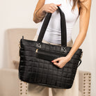 Person holding a black quilted travel tote against a neutral background