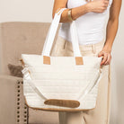 White tote bag with brown accents held by a person in a neutral setting