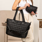 Person holding a black quilted travel tote and clutch in a neutral setting