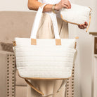 Soft white quilted tote bag with beige accents held by a person in a neutral setting