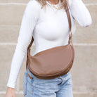 Person wearing a brown vegan leather crossbody bag with a blurred background