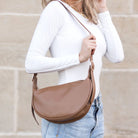 Person wearing a brown shoulder bag against a beige wall