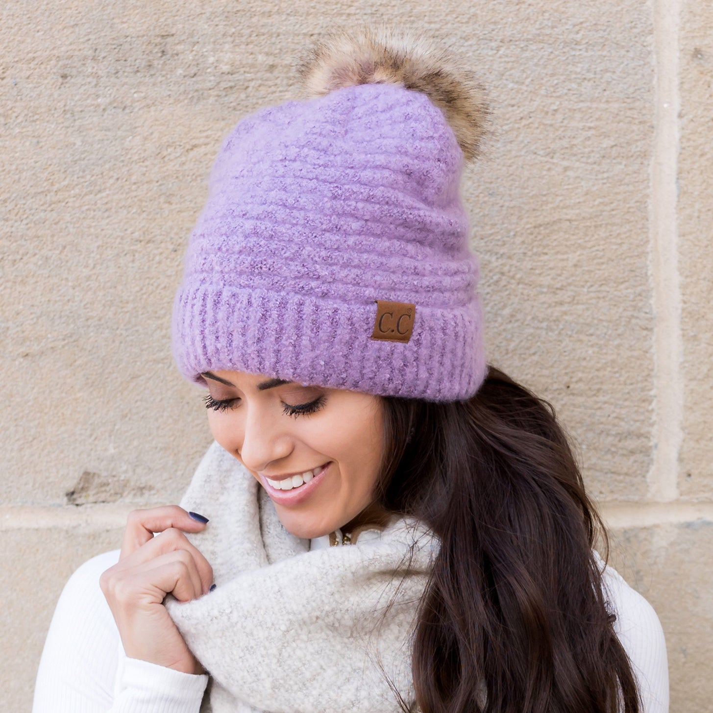 Lavender boucle knit hat with faux fur pom worn with scarf, angled view